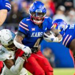 Nov 23, 2024; Kansas City, Missouri, USA; Kansas running back Devin Neal (4) attempts to break through the tackle of Colorado safety Carter Stoutmire (23) during the 3rd quarter between the Kansas Jayhawks and the Colorado Buffaloes at GEHA Field at Arrowhead Stadium.