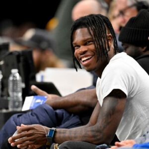 Heisman Trophy winner Travis Hunter Jr. laughs during the second half of the game between the Dallas Mavericks and the Minnesota Timberwolves at the American Airlines Center.