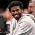 Jan 14, 2025; Dallas, Texas, USA; Colorado Buffaloes quarterback Shedeur Sanders laughs as he watches the game between the Dallas Mavericks and the Denver Nuggets during the second half at the American Airlines Center.
