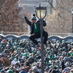 A fan of the Philadelphia Eagles climbs a light pole during the Super Bowl LIX championship parade and rally.