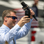Jul 31, 2022; Indianapolis, Indiana, USA; Dale Earnhardt Jr. raises his hands to cheering fans on the grid before the Verizon 200 at the Indianapolis Motor Speedway Road Course. Mandatory Credit: Marc Lebryk-Imagn Images