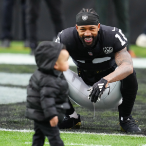Jan 5, 2025; Paradise, Nevada, USA; Las Vegas Raiders cornerback Jack Jones (18) plays with his son before the start of a game against the Los Angeles Chargers at Allegiant Stadium. Mandatory Credit: Stephen R. Sylvanie-Imagn Images