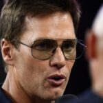 Retired Hall of Fame New England Patriot player Tom Brady talks with Brian Hoyer during the first half of a game against the Washington Commanders at Gillette Stadium.