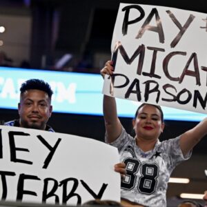 Dallas Cowboys fans hold up signs to owner Jerry Jones and defensive end Micah Parsons (11) during the second half of the game against the Baltimore Ravens at AT&T Stadium.