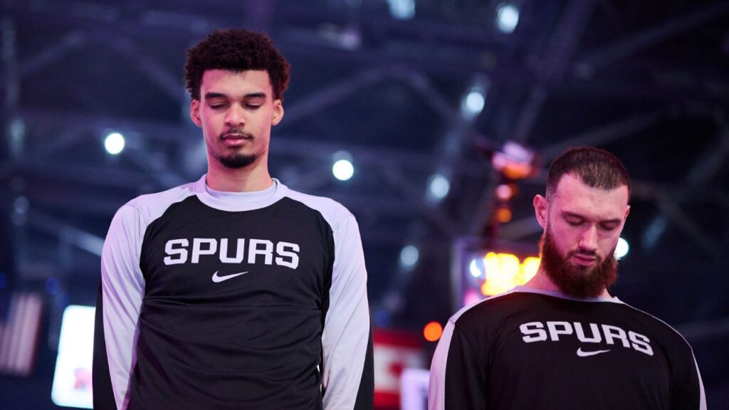 Dec 13, 2024; Portland, Oregon, USA; San Antonio Spurs center Victor Wembanyama (1), left, stands with forward Sandro Mamukelashvili (54) during the singing of the national anthem before a game against the Portland Trail Blazers at Moda Center. Mandatory Credit: Troy Wayrynen-Imagn Images