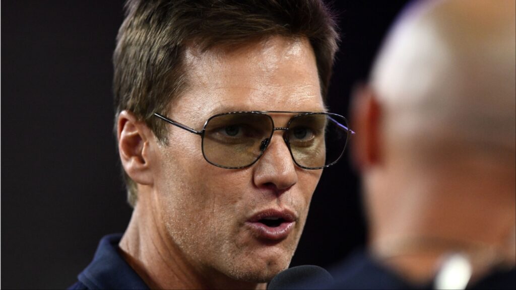Retired Hall of Fame New England Patriot player Tom Brady talks with Brian Hoyer during the first half of a game against the Washington Commanders at Gillette Stadium.
