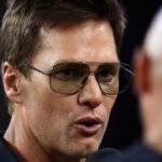 Retired Hall of Fame New England Patriot player Tom Brady talks with Brian Hoyer during the first half of a game against the Washington Commanders at Gillette Stadium.