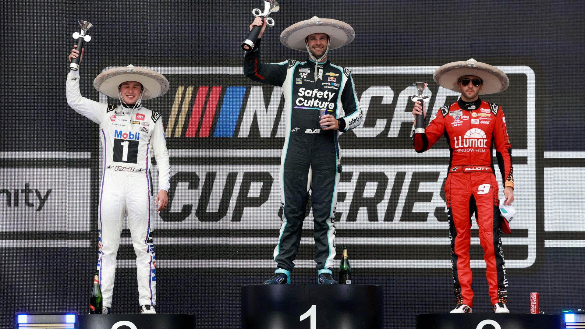 Shane Van Gisbergen celebrates on the podium after winning the NASCAR Cup Series Mexico alongside second place driver Christopher Bell and third place driver Chase Elliott during the NASCAR Cup Series Mexico City Race at Autodromo Hermanos Rodriguez.