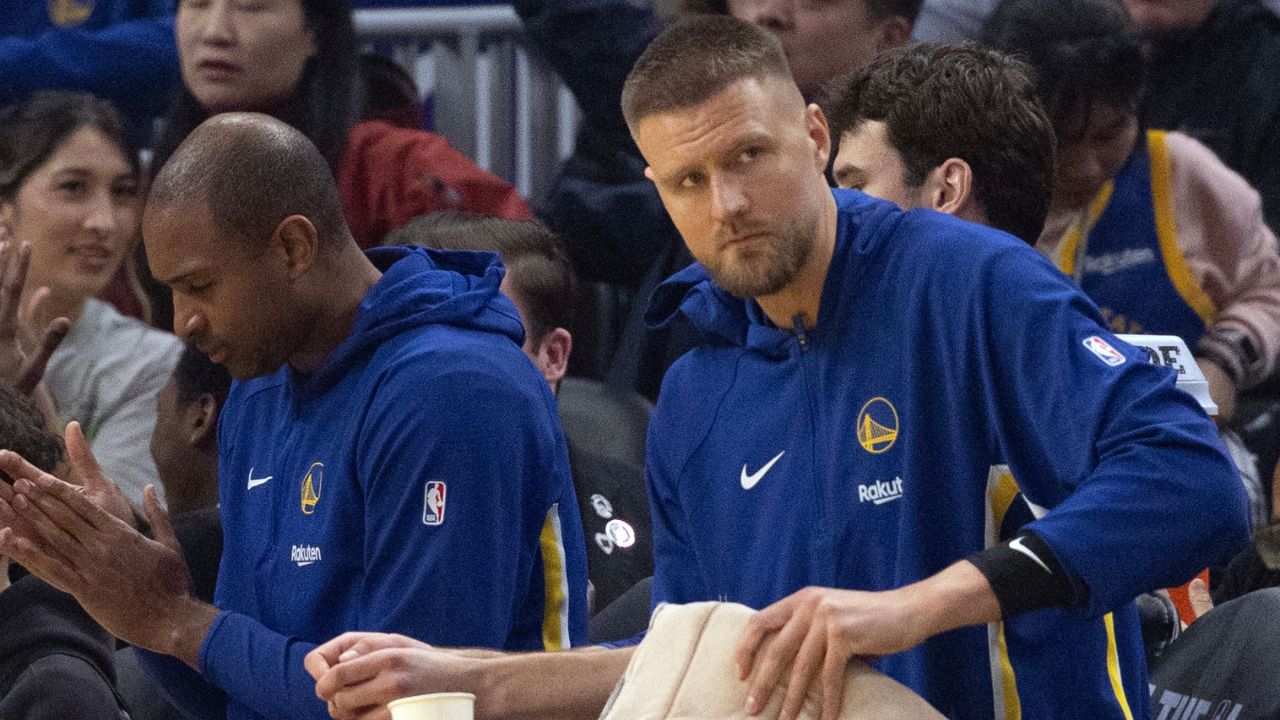 New Golden State Warriors forward Kristaps Porzingis (with towel) watches the action against the Boston Celtics from the bench during the first quarter at Chase Center
