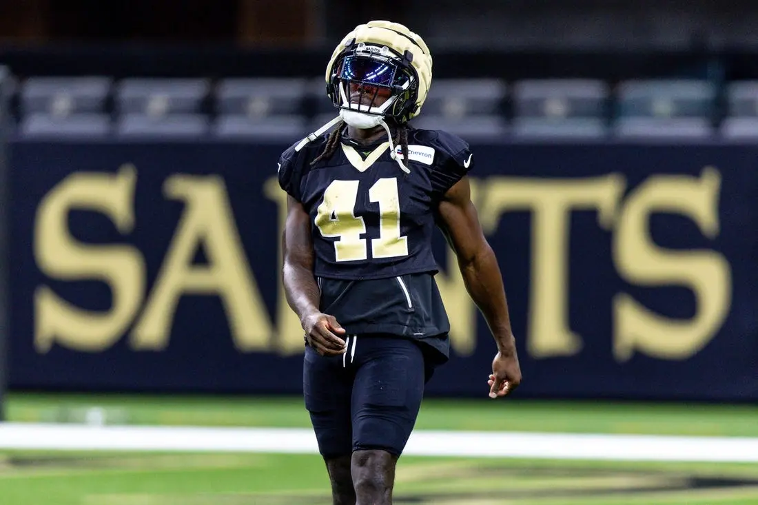 Alvin Kamara practicing in a black New Orleans Saints jersey with logo in the background.