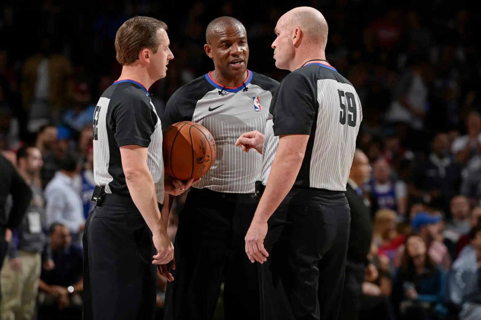 Three NBA referees discussing with a basketball during a game.
