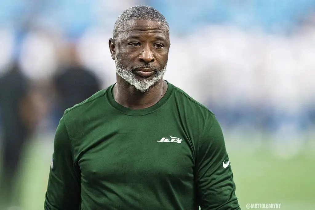 Aaron Glenn wearing a green Jets shirt on the field during an NFL game.