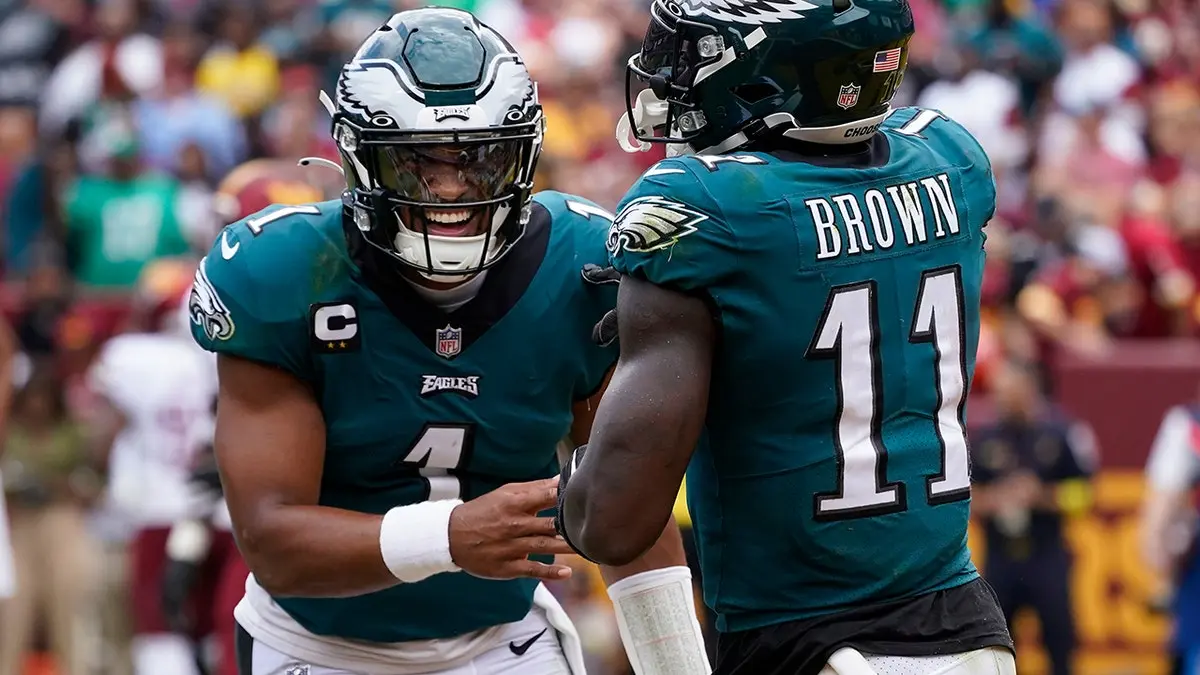 Jalen Hurts and A.J. Brown celebrating on the field in Eagles uniforms.