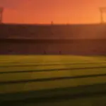 Floodlit stadium pitch at golden-hour with empty turf, packed stands, and national flag colour atmosphere.