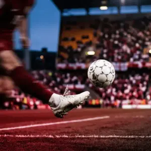 Floodlit stadium with crimson and white colour scheme, footballer mid-kick with motion blur, evening atmosphere.