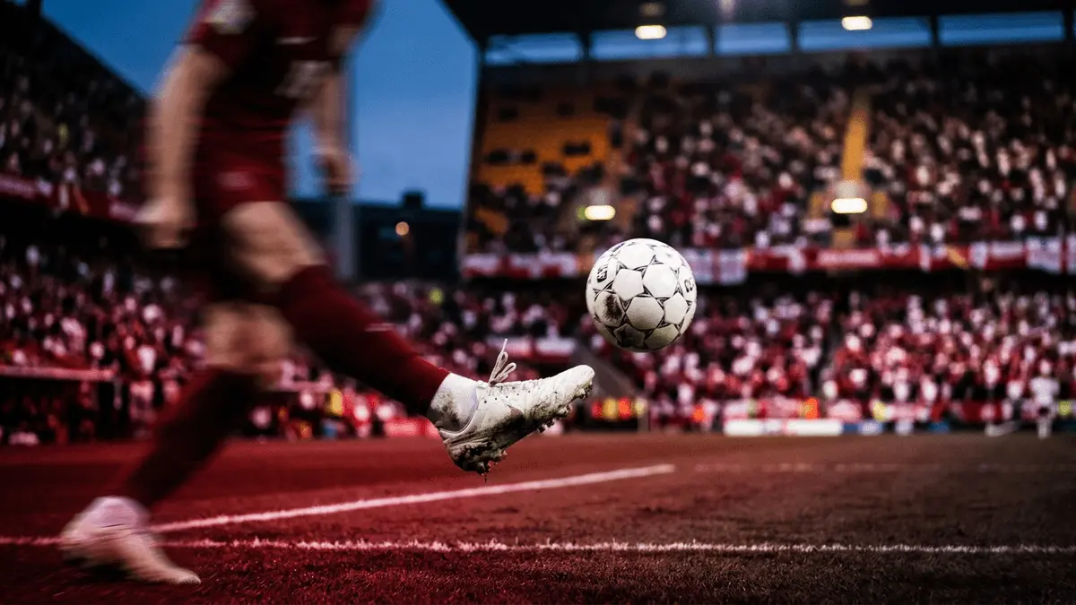 Floodlit stadium with crimson and white colour scheme, footballer mid-kick with motion blur, evening atmosphere.