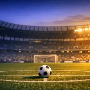 Floodlit stadium pitch at dusk with blue-tinted shadows, football on centre spot, goal net in background.