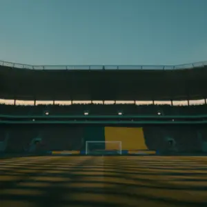 Empty floodlit stadium pitch at dusk with dramatic shadow patterns and packed stands in background