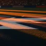 Empty floodlit stadium pitch at golden-hour with shadow patterns and crowd bokeh in background.