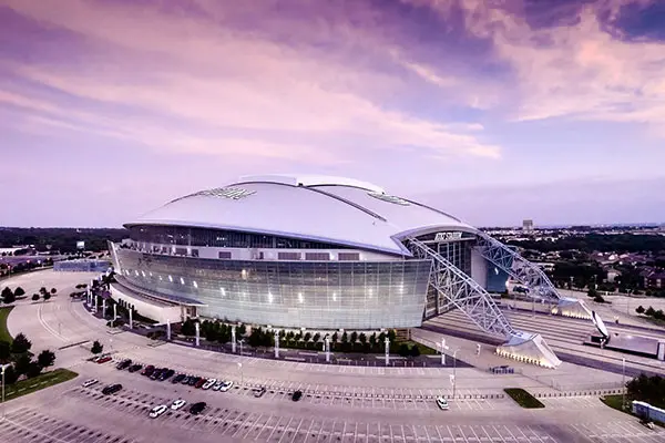 Exterior view of AT&T Stadium in Arlington, Texas, under a colorful sky.