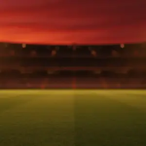 Empty floodlit stadium at dusk with dramatic shadows and golden-hour lighting creating atmospheric match preview mood.