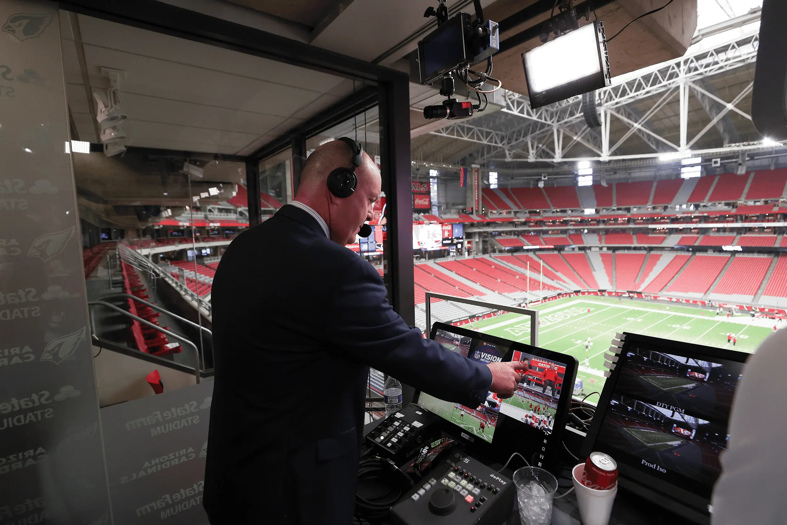 Broadcast booth with a commentator analyzing video feeds during a football game.