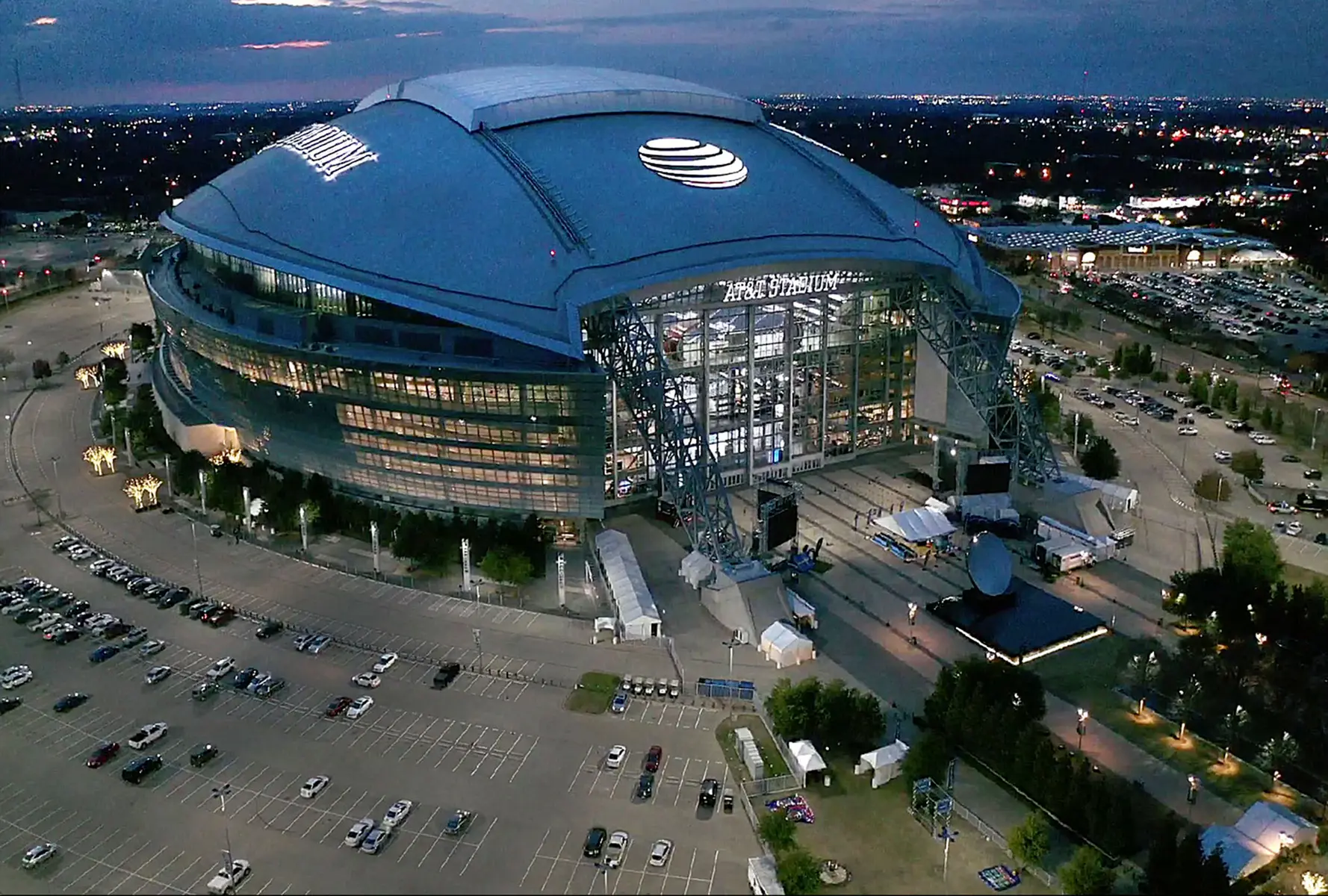 Aerial evening view of AT&T Stadium, home of the Dallas Cowboys, featuring the lighted exterior and parking lots.