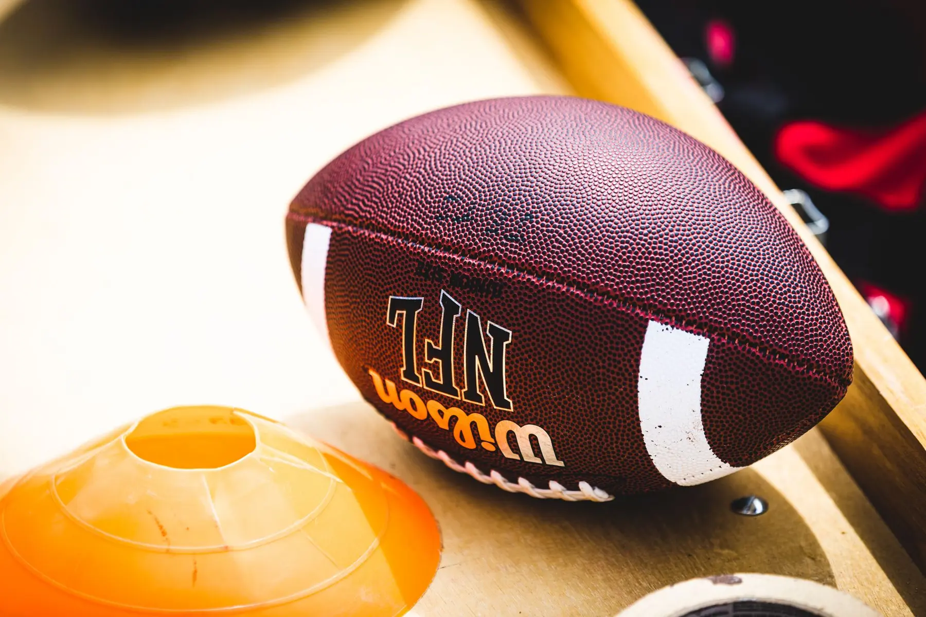 Close-up of a Wilson NFL football resting on a wooden surface next to an orange training cone.