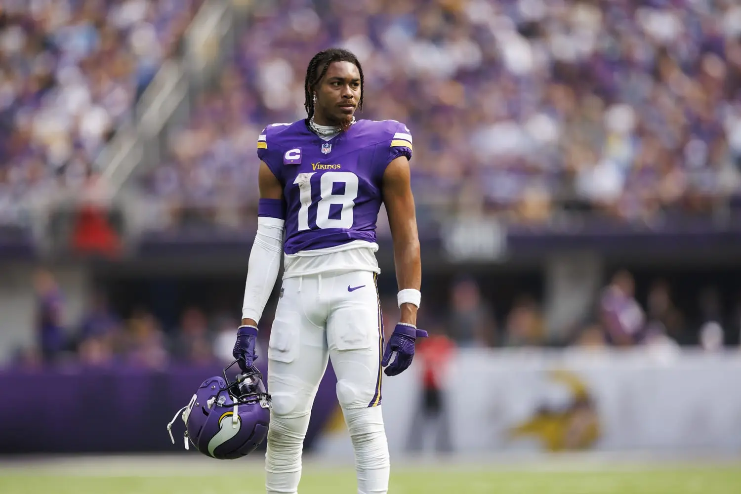 Justin Jefferson of the Minnesota Vikings wearing a purple jersey number 18, holding his helmet on the field.